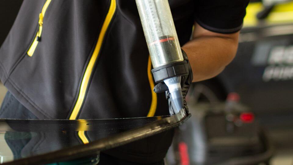 Gros plan du tirage d'un cordon de colle sur un pare-brise