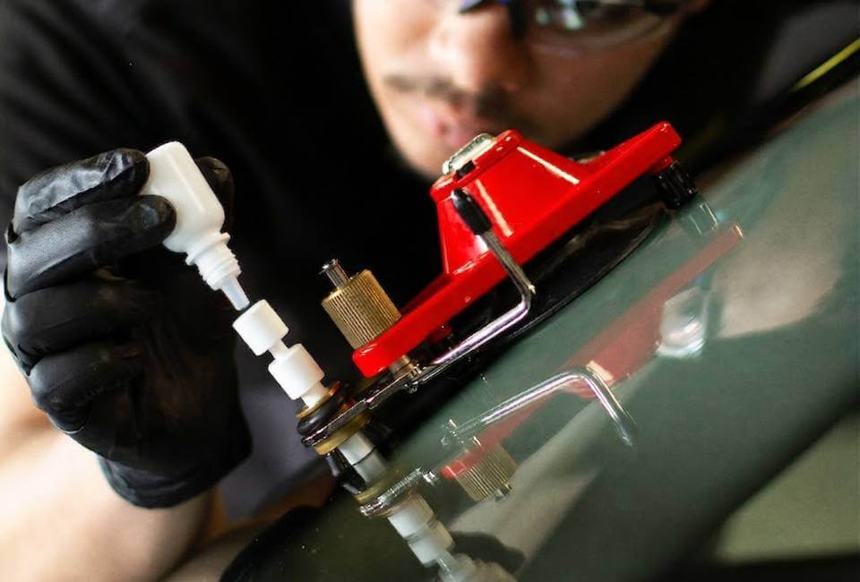 Technicien vitrage réparant un impact sur un pare-brise