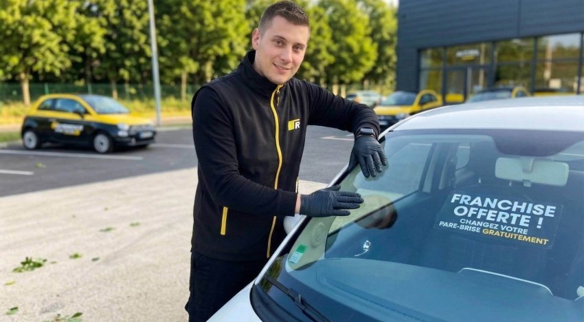 Technicien vitrage devant un pare-brise neuf qui vient d'être changé gratuitement